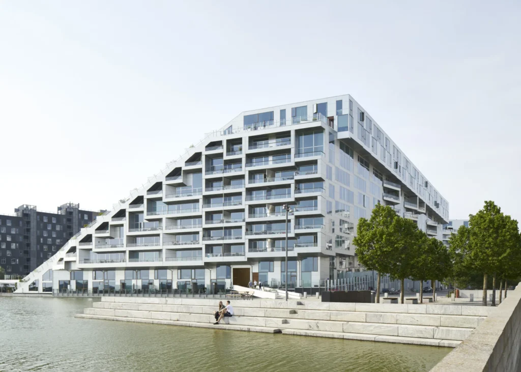8 House by Bjarke Ingels Group with the Ørestad landscape beyond and people sitting by the water with trees