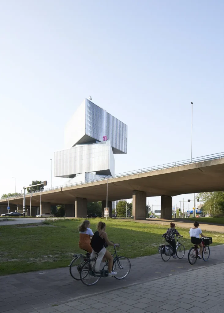 Cyclists passing nHow Amsterdam RAI Hotel by OMA / Rem Koolhaas on Zuidas avenue