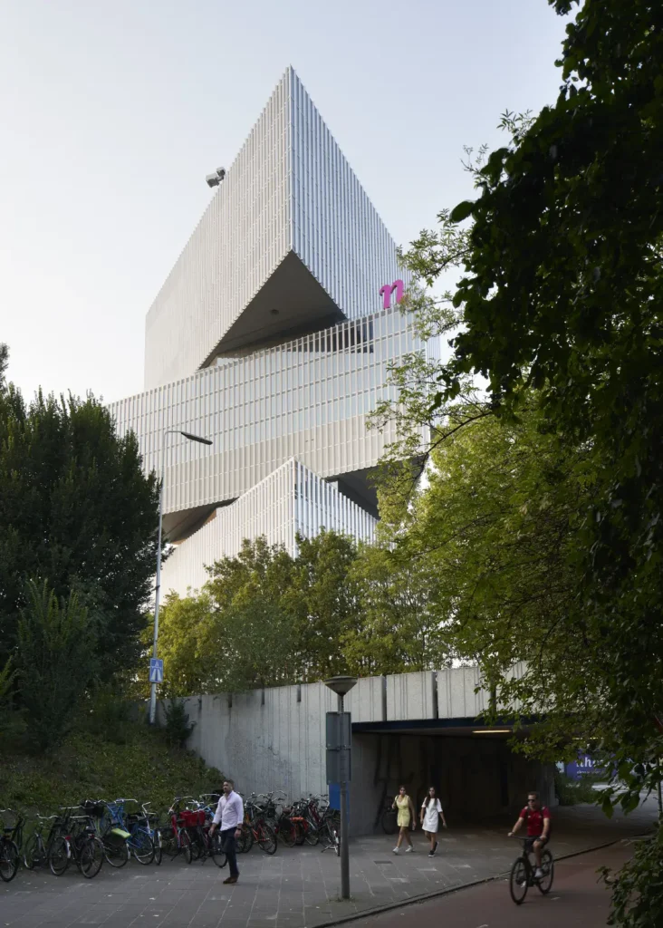 Pedestrians with nHow hotel framed by trees with Zuidas business district behind