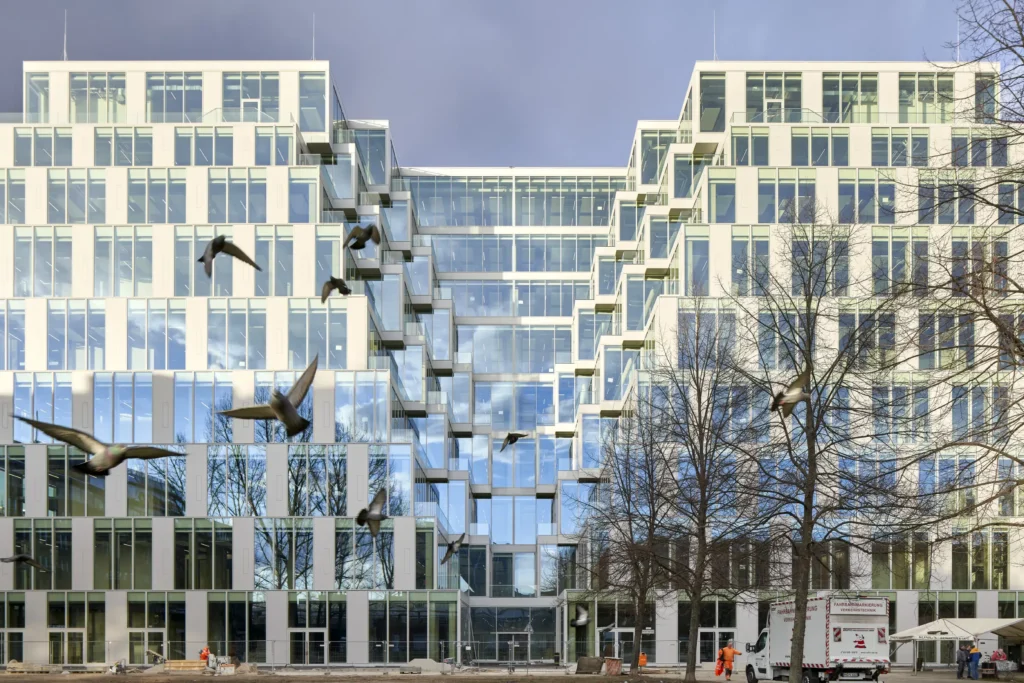 Pidgeons flkying in front of UP! Berlin with illuminated glass facade by Jasper Architects