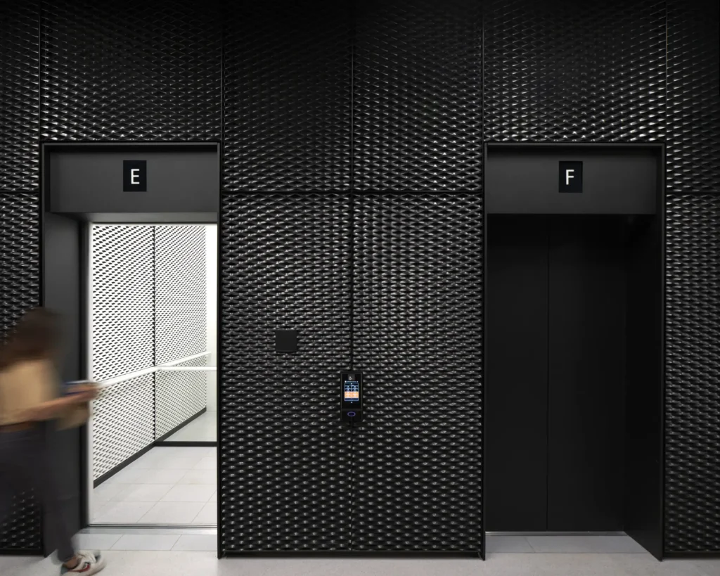 person entering lift inside with perforated metal walls at UP! Berlin by Jasper Architects