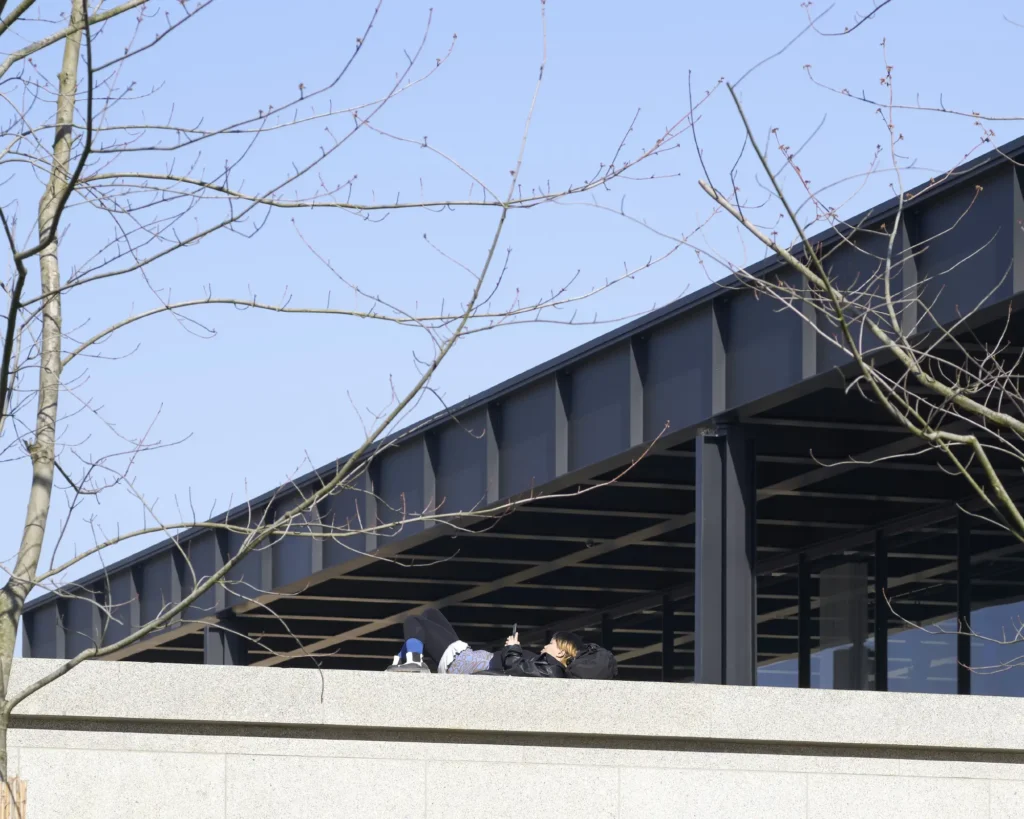 Steel roof and granite podium detail at the Neue Nationalgalerie by Mies van der Rohe with woman reading