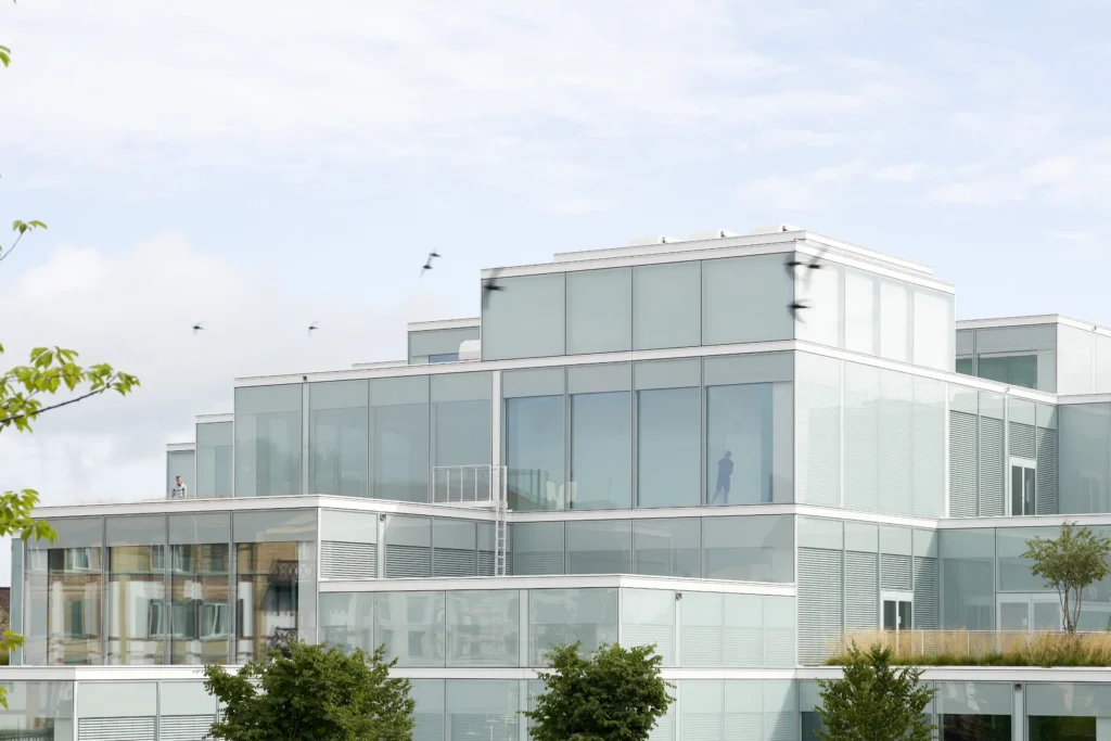 Rooftop garden with birds flying in front of the stacked glass volumes of the SQUARE Learning Center