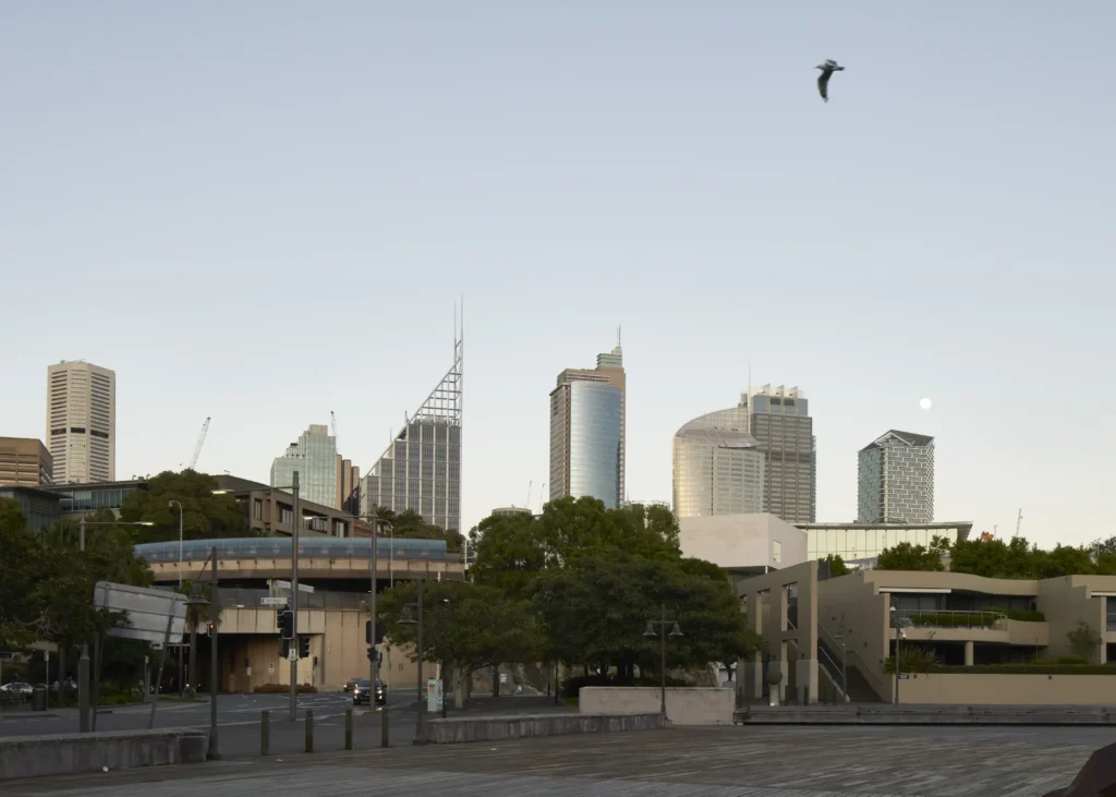 Distant view of Sydney Modern pavilions set among parkland with city behind and rising moon
