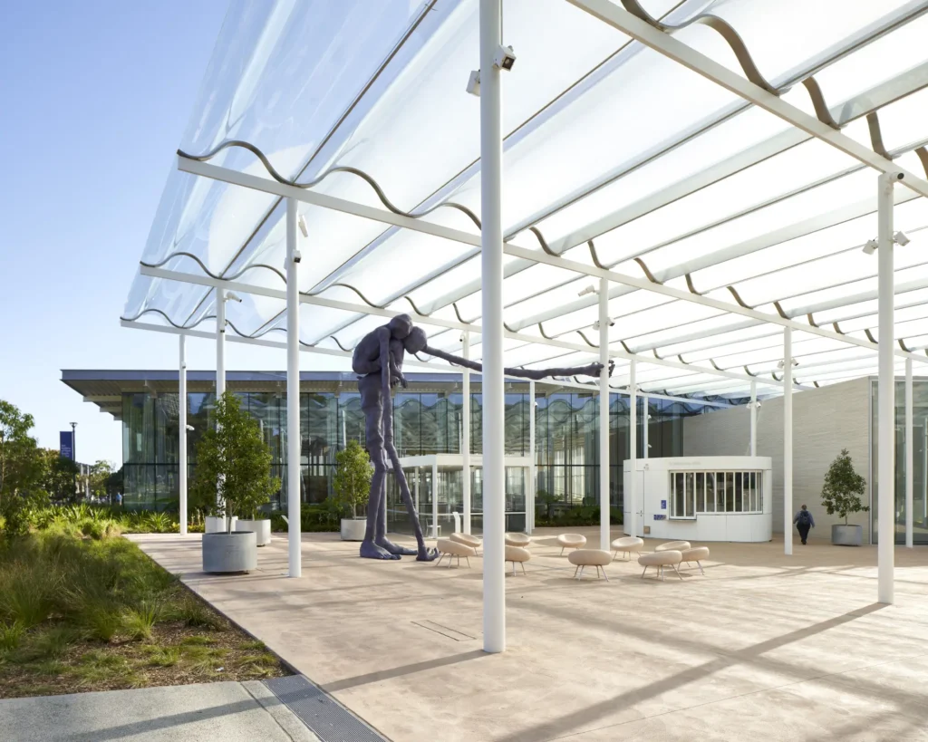 Outdoor sculpture terrace with bronze figures beneath glass canopy at Sydney Modern