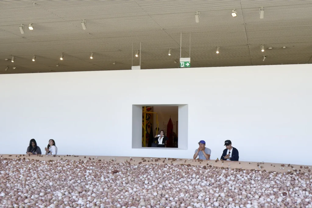 Visitors at a oval table with art installation in expansive gallery with geometric ceiling at Sydney Modern