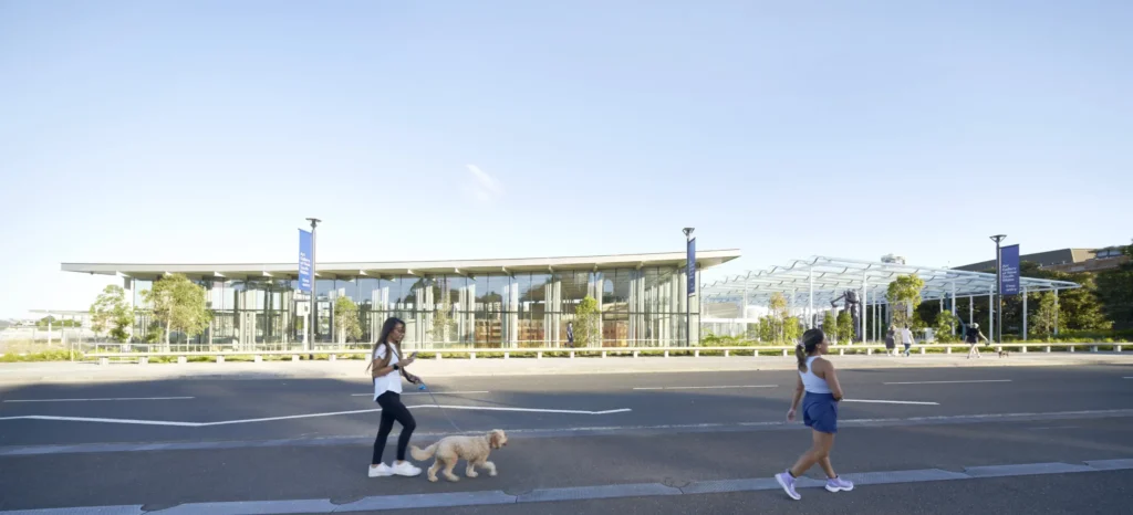 Morning walkers in front of the crystalline glass facade of Sydney Modern reflecting landscape by SANAA architects