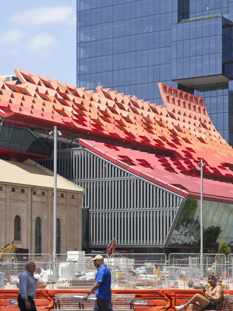 Geometric red metal canopy of PHIVE with urban life in frontand glass towers behind