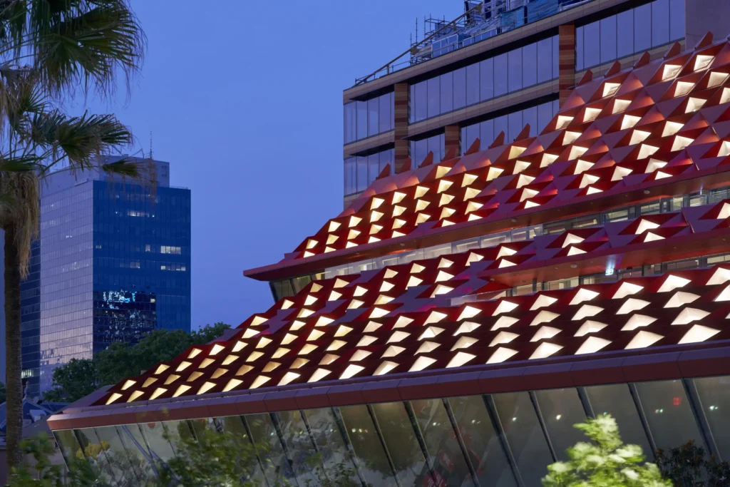 Night view of diamond-patterned roof at PHIVE with glass towers reflected behind