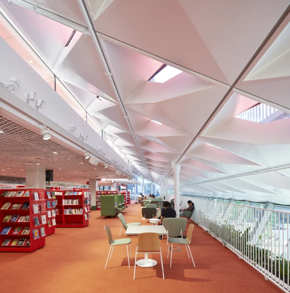 Library seating area with green lounge chairs beneath triangular ceiling panels at PHIVE