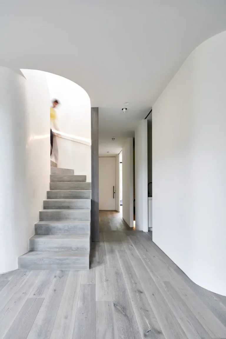 Person descending the dark ash staircase in light-filled hallway at Alexandra Street South Yarra