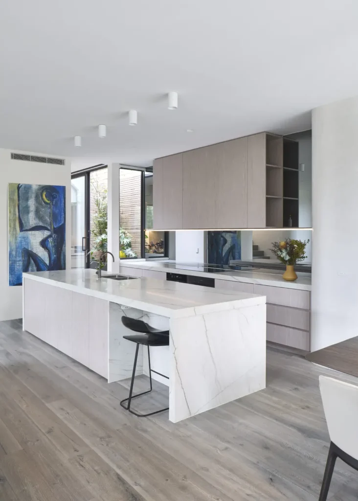 Open-plan kitchen with stone island bench and blue artwork at Alexandra Street by Megowan Architectural
