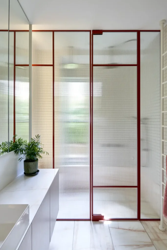 Bathroom with red-framed glass partition and minimalist white finishes at Lindsay house Melbourne