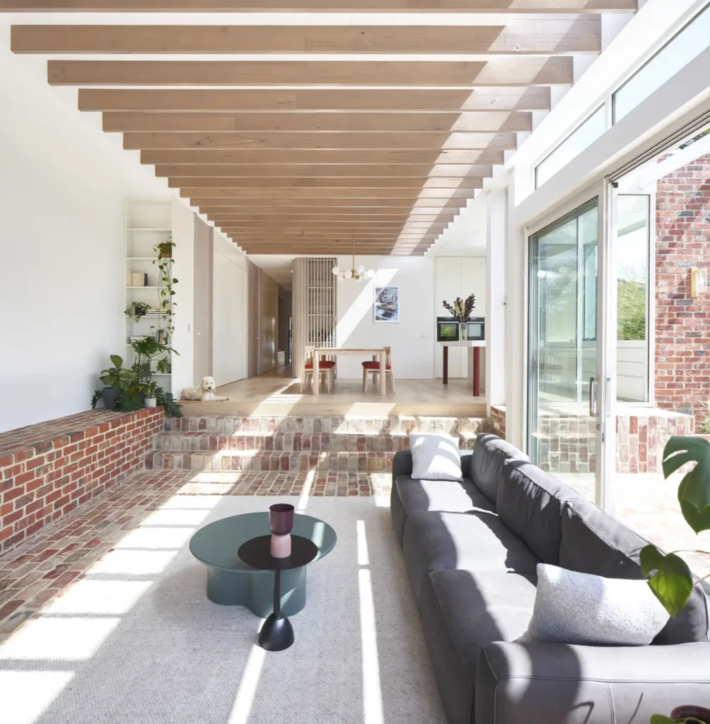 Open-plan living and dining area in Lindsay house with exposed timber rafters and brick feature wall