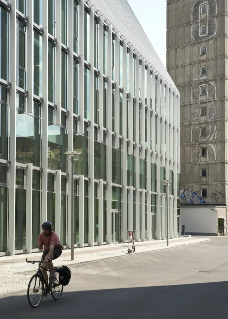 Cyclist passing Pressehaus am Alexanderplatz with green glass facade by GMP Architects