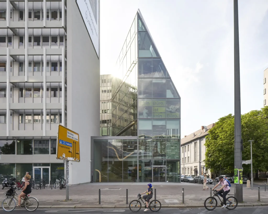 Cyclist pass the podium building with vertical glass fins at Pressehaus am Alexanderplatz by GMP Architects