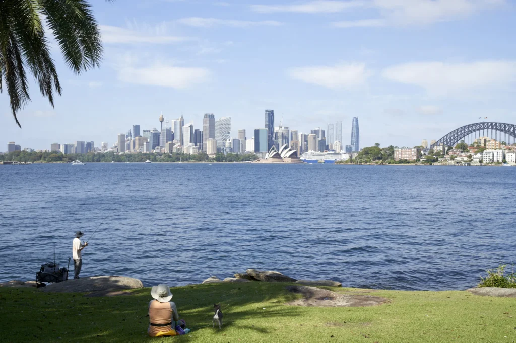 Boy fishing and sydney harbour skyline with Quay Quarter Tower among the CBD high-rises