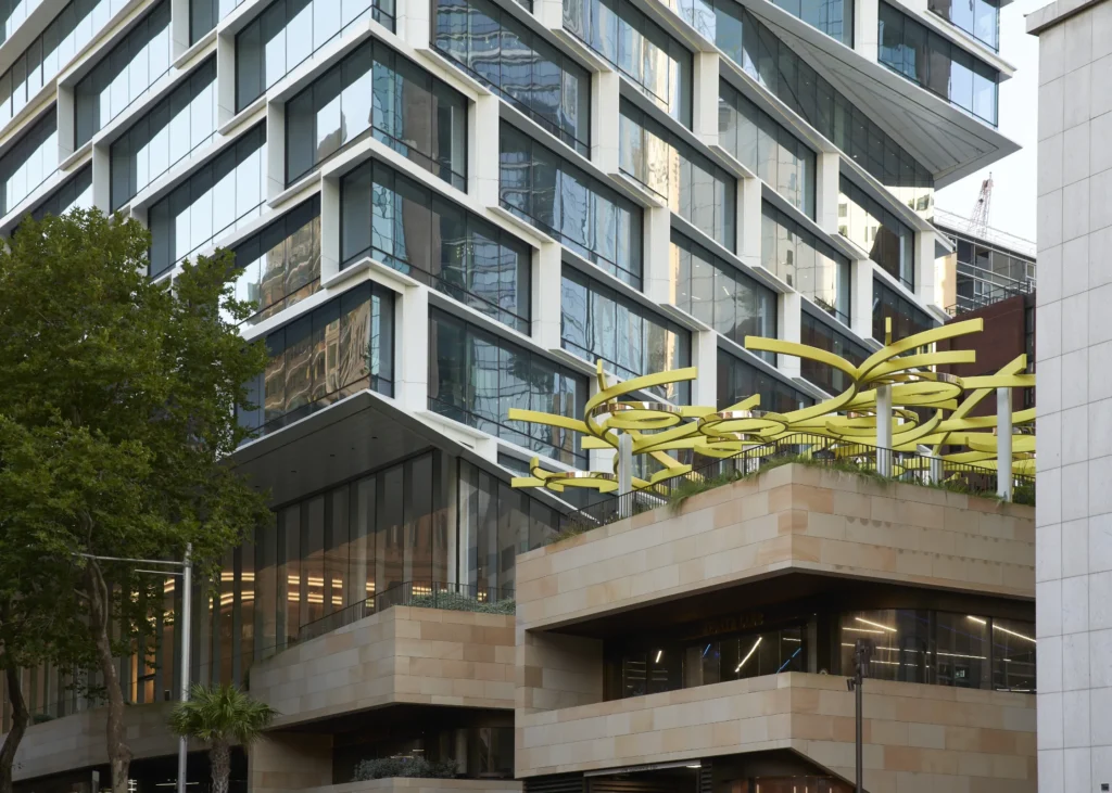 Quay Quarter Tower in Sydney seen from street level, sandstone volumes, glass facade and yellow canopy sculpture