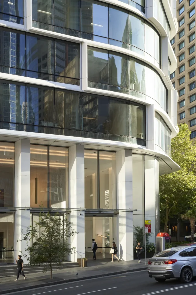 Pedestrians passing the curved glass facade of Quay Quarter Tower in Sydney