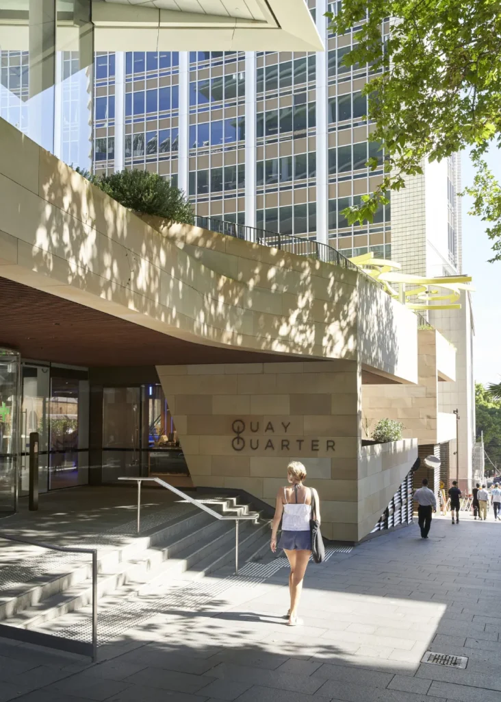 Sandstone podium and canopy of Quay Quarter Tower with pedestrians in Sydney